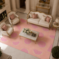 A luxury living room scene featuring a large pink area rug with a repeating watermelon slice pattern, styled with cream-colored armchairs, a matching sofa, and a marble coffee table.