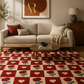 A red and cream checkered area rug with a repeating heart and rose pattern, styled in a warm, modern living room setting with a beige sofa, wooden coffee table, and neutral decor.