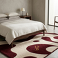 Bedroom with a wooden bed, white bedding, and a patterned rug with a logo.