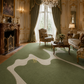 A large green area rug with an abstract organic pattern in cream and olive tones, styled in a luxurious, ornate vintage living room with gold-trimmed walls, a fireplace, and matching green drapery.