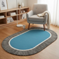 Blue oval rug with striped border in a room with a gray armchair and wooden bookshelf.