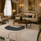 A luxury living room featuring a large cream and navy abstract-patterned area rug under a dark wood coffee table, with a matching beige sofa and armchair in an ornate gold-trimmed room.