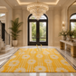 A large yellow and white floral area rug displayed in a luxurious, high-ceilinged entryway with marble floors, a crystal chandelier, and a console table.