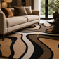 A modern living room scene featuring a large area rug with an abstract wavy pattern in beige, brown, black, and cream, styled under a light beige sofa.