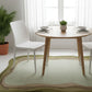Dining area with a round wooden table and white chairs on a green rug.