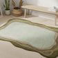 Decorative rug with wavy design on a wooden floor, with a bench and plants in the background.