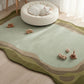 Cat lying on a round cushion on a green and brown patterned rug with toys around.