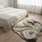 Abstract patterned rug on a wooden floor in a bedroom with white bedding and curtains.