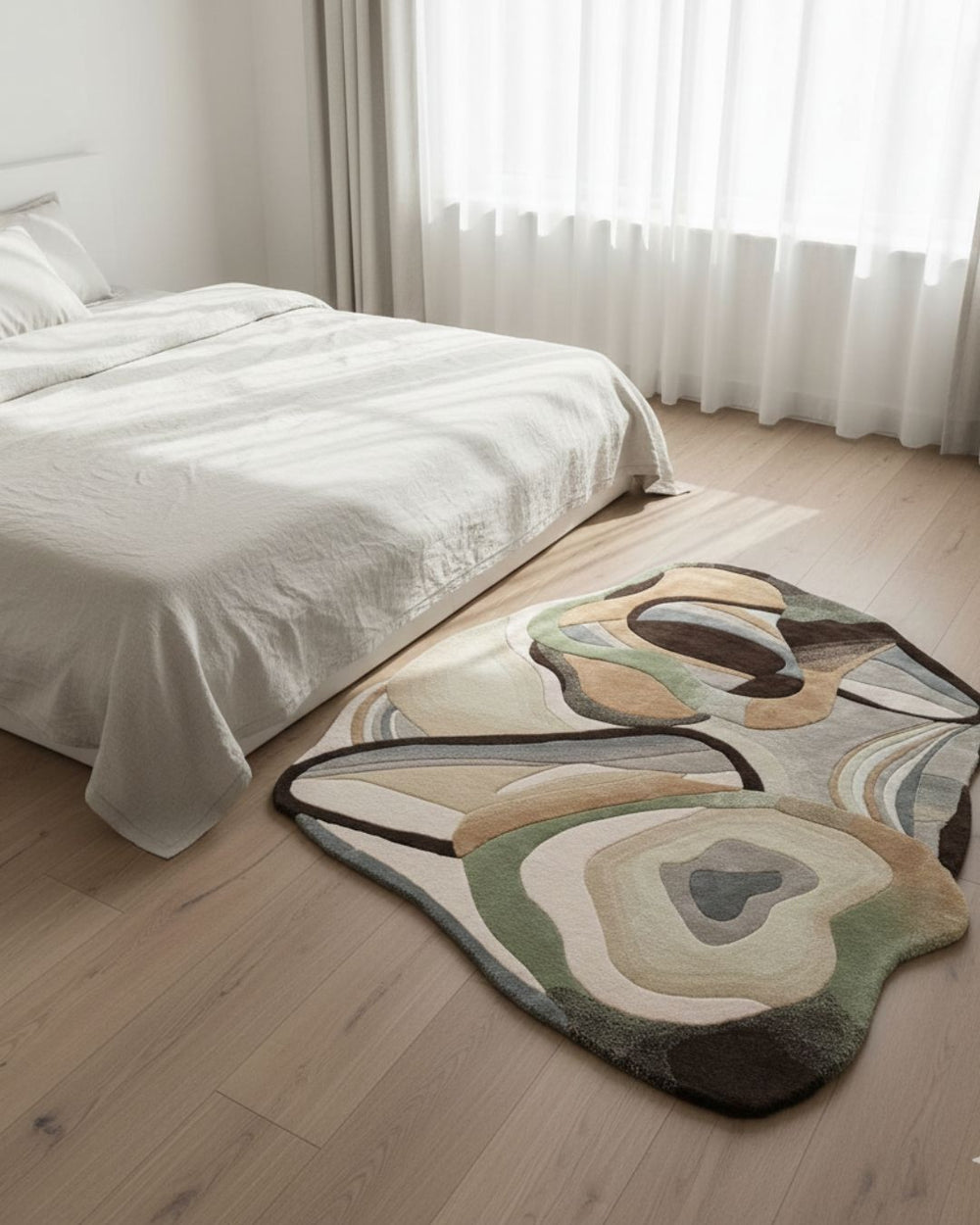 Abstract patterned rug on a wooden floor in a bedroom with white bedding and curtains.