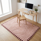 Wooden desk with chair and computer setup on a pink patterned rug in a room with a window.