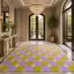 A large rectangular area rug with a purple and lime green checkered pattern and white starburst accents, displayed in a grand, elegant foyer with marble floors, a crystal chandelier, and arched glass doors.