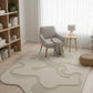 Living room with a beige rug, gray armchair, and wooden bookshelf.