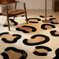 Patterned rug with black and beige shapes on a floor with a wooden chair and lamp.