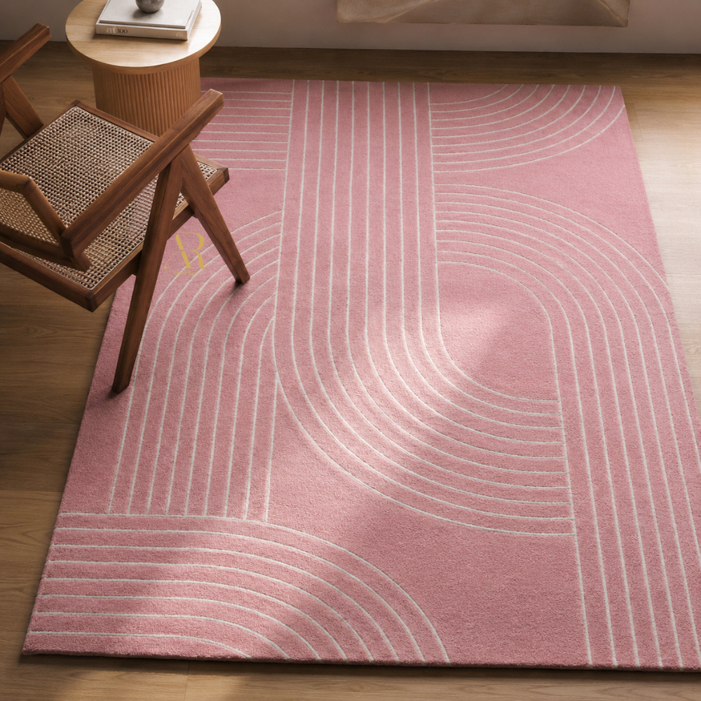 A pink area rug with a white geometric arch pattern, styled on a wooden floor next to a wooden chair and a small side table.