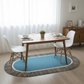 Dining area with a wooden table and white chairs on a blue oval rug.