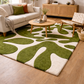Living room with a green and white patterned rug, beige sofa, and wooden coffee table.
