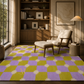 A large area rug with a purple and lime green checkerboard pattern and white starburst motifs, styled in a warm, modern living room with a mid-century armchair and wooden bookshelves.