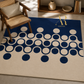 A rectangular area rug with a cream and navy blue geometric pattern of interlocking circles, styled in a modern living room setting next to a wooden armchair.