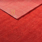 A close-up of a red textured rug or carpet with a folded corner showing the pile and edge, photographed against no separate background because the product fills the frame.