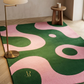 Pink and green abstract rug with a gold logo on a wooden floor.