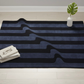 Navy blue and black striped rug on a light wood floor with a plant and books.