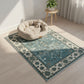 Decorative rug with a floral pattern on a wooden floor, featuring a pet bed and plant in the background.