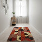 Colorful geometric rug on a light wooden floor with a small table and plant in the corner.