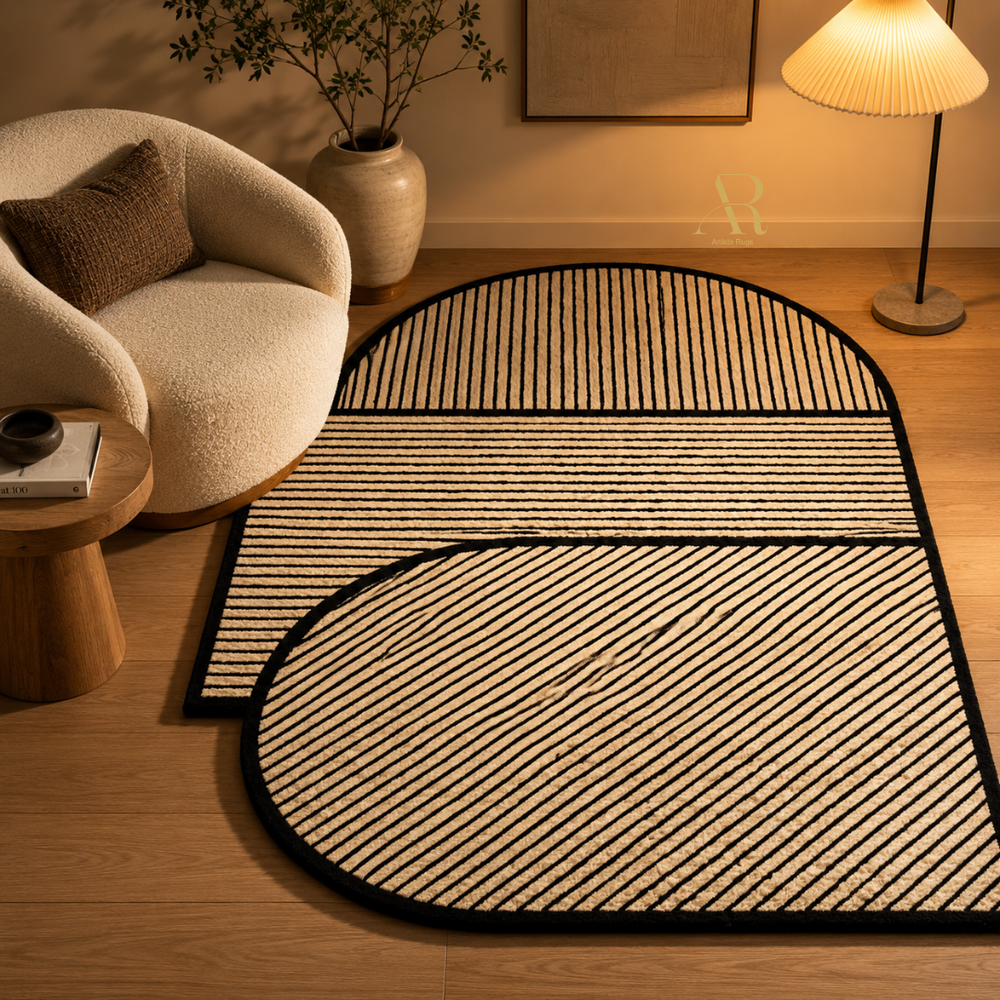 A modern geometric area rug with a slatted natural fiber pattern and black trim, styled in a warm, contemporary living room next to a cream-colored armchair and a lit floor lamp.