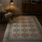 Patterned rug in a dimly lit room with a chair and lamp.