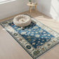 Decorative blue rug with intricate patterns on a wooden floor, featuring a pet bed and small table.