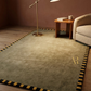 Living room with a green rug, wooden side table, and beige sofa.