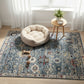 Dog bed on a patterned rug with a small table and plant in the background