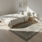 Neatly made bed in a bright bedroom with a patterned rug on the floor.