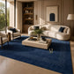 A large navy blue area rug with a cream dotted border pattern is styled in a modern living room with a cream curved sofa, matching armchairs, and a light wood coffee table.