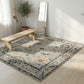 Decorative rug with floral patterns on a wooden floor, with a bench and plant in the background.