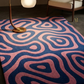 Patterned pink and blue rug on a dark floor with a lamp and chair in the background.