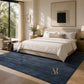 A large navy blue textured area rug in a modern, sunlit bedroom with a beige bed, white linens, wooden nightstands, and a large framed abstract print on the wall.