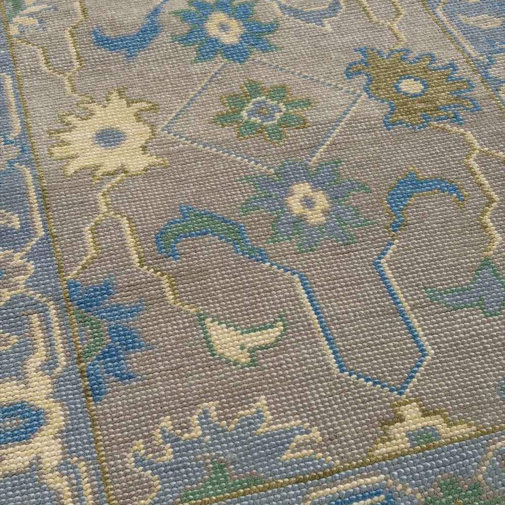 Close-up of a patterned rug with floral designs in blue, green, and beige on a gray background.
