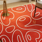 Red rug with white abstract patterns on a wooden floor.