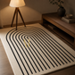 A cream-colored area rug with a bold black arched stripe pattern, styled in a warm, modern living room next to a wooden floor lamp and a low wooden console table.