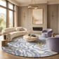 A luxury modern living room featuring a large round area rug with a wavy light blue and white pattern, styled with a curved cream sofa, purple accent chairs, and a marble coffee table.