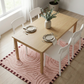 Dining table set with plates, cutlery, and a vase of flowers on a pink rug in a bright room.