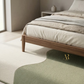 Bed with wooden frame and beige bedding in a minimalistic bedroom.