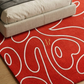 Red rug with white patterns and a logo on a wooden floor.