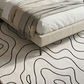 Beige bed with a patterned rug featuring abstract line designs.