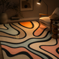 A modern area rug with an abstract wavy pattern in beige, black, peach, and light blue, styled in a cozy living room next to a white armchair and a lit floor lamp.