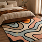 A modern area rug with an abstract wavy pattern in beige, light blue, peach, and black, styled on a wooden floor in a bedroom setting under a bed.
