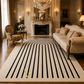 A large rectangular area rug with a cream background and bold black vertical stripe pattern, styled in a luxurious, elegant room with a fireplace, chandelier, and vintage furniture.