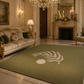 A large olive green area rug with a white palm leaf and circle motif, displayed in a luxurious, ornate vintage-style living room with a fireplace, chandelier, and cream sofa.