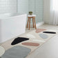 Bathroom with a colorful abstract rug on the floor, a bathtub, and a stool with a plant.
